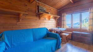 A wooden cabin interior with a blue sofa, a small table, and a window offering a view of the outdoors.