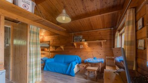 A cozy cabin interior with wooden walls, a blue sofa, a small table, and a bunk bed.