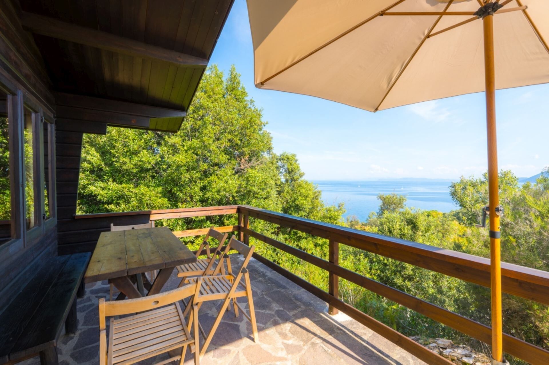 A wooden deck with a table and chairs, overlooking a scenic view of the sea and greenery.
