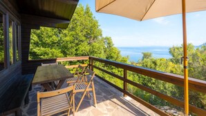A wooden deck with a table and chairs, overlooking a scenic view of the sea and greenery.