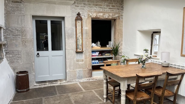 A stone-walled room with a wooden table and chairs, a white door, and a bookshelf filled with books and decorative items. - Beautiful Grade II listed house with stunning uninterrupted views. Sleeps 8 (Carlton-in-Coverdale, Leyburn, Yorkshire)