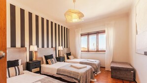Ein Hotelzimmer mit zwei Betten, einem Vorhangfenster, Holzboden und einer kleinen Bank.