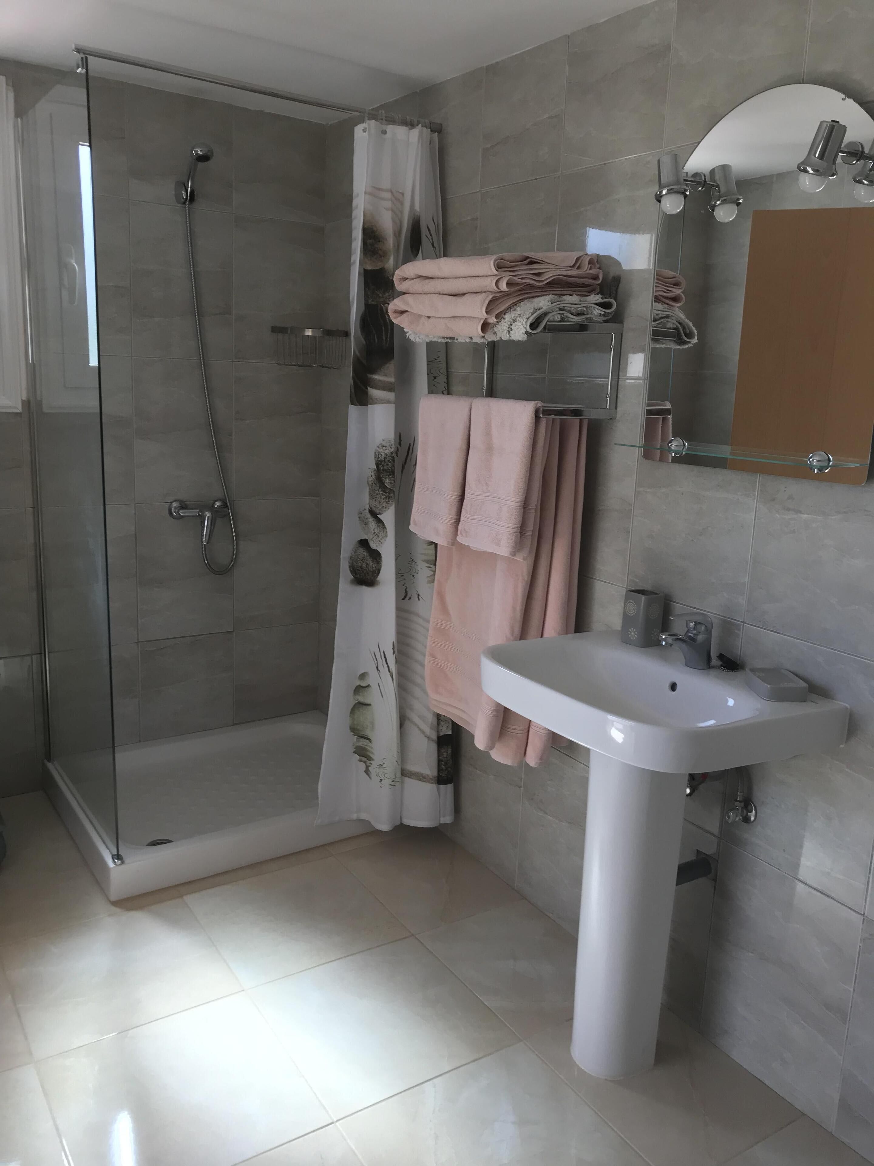 Une salle de bain moderne avec une douche à parois de verre, un lavabo blanc et un porte-serviettes où sont soigneusement pliées les serviettes.