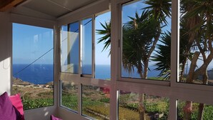 A room with large windows overlooking a coastal landscape, including palm trees and a view of the sea. - AMAZING VIEWS OF ATLANTIC & TEIDE WITH PRIVATE TERRACE , POOL & BBQ (Buen Paso)