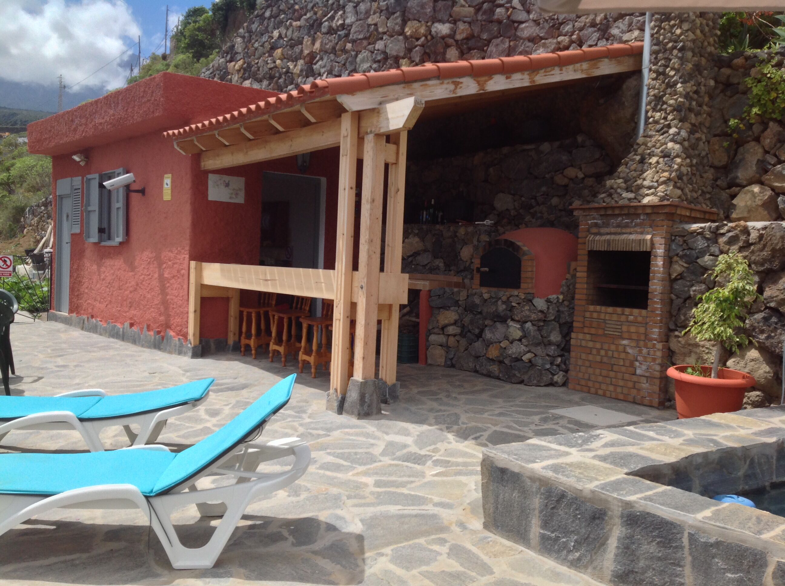 Un edificio rojo con fachada de piedra, una pérgola de madera y una zona con bancos de piedra.