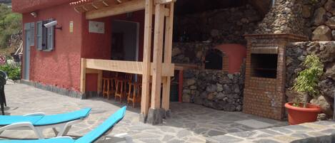 Un edificio rojo con fachada de piedra, una pérgola de madera y una zona con bancos de piedra.