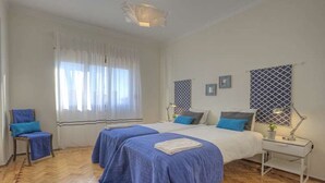 A bedroom with two beds, a chair, a nightstand, and a window with curtains.