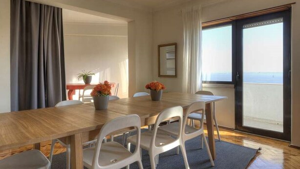A dining area with a wooden table, white chairs, and potted plants.