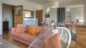 A cozy living room with a sofa, a chair, a dining area with a table and chairs, and a kitchen in the background.