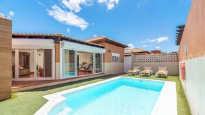 Un patio trasero con piscina, un porche cubierto y un edificio blanco con puertas de vidrio correderas.