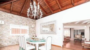 Un comedor con una mesa redonda, sillas blancas, una araña y una pared de piedra.