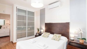Una habitación de hotel con una cama grande, una puerta corrediza al baño, un cabecero de madera y una mesita de noche pequeña con una lámpara y una planta.