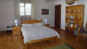 A bedroom with a wooden bed, two bedside tables with lamps, a wooden wardrobe, and a window with curtains. - Magnificent sea and mountain views from the roof terrace. Quiet and restful place (Morc. Anna, Flic en Flac)