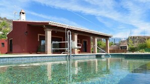 Une piscine à l’eau d’un bleu limpide, un bâtiment rouge avec un toit en tuiles et une cheminée.