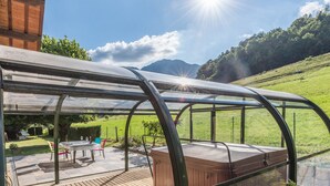 Eine überdachte Terrasse im Freien mit Whirlpool, Holzterrasse und Blick auf eine grüne Landschaft.