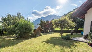 Ein Rasen mit einer Holzwieländeranlage, einer kleinen Werkstatt und einem Haus mit rotem Dach.