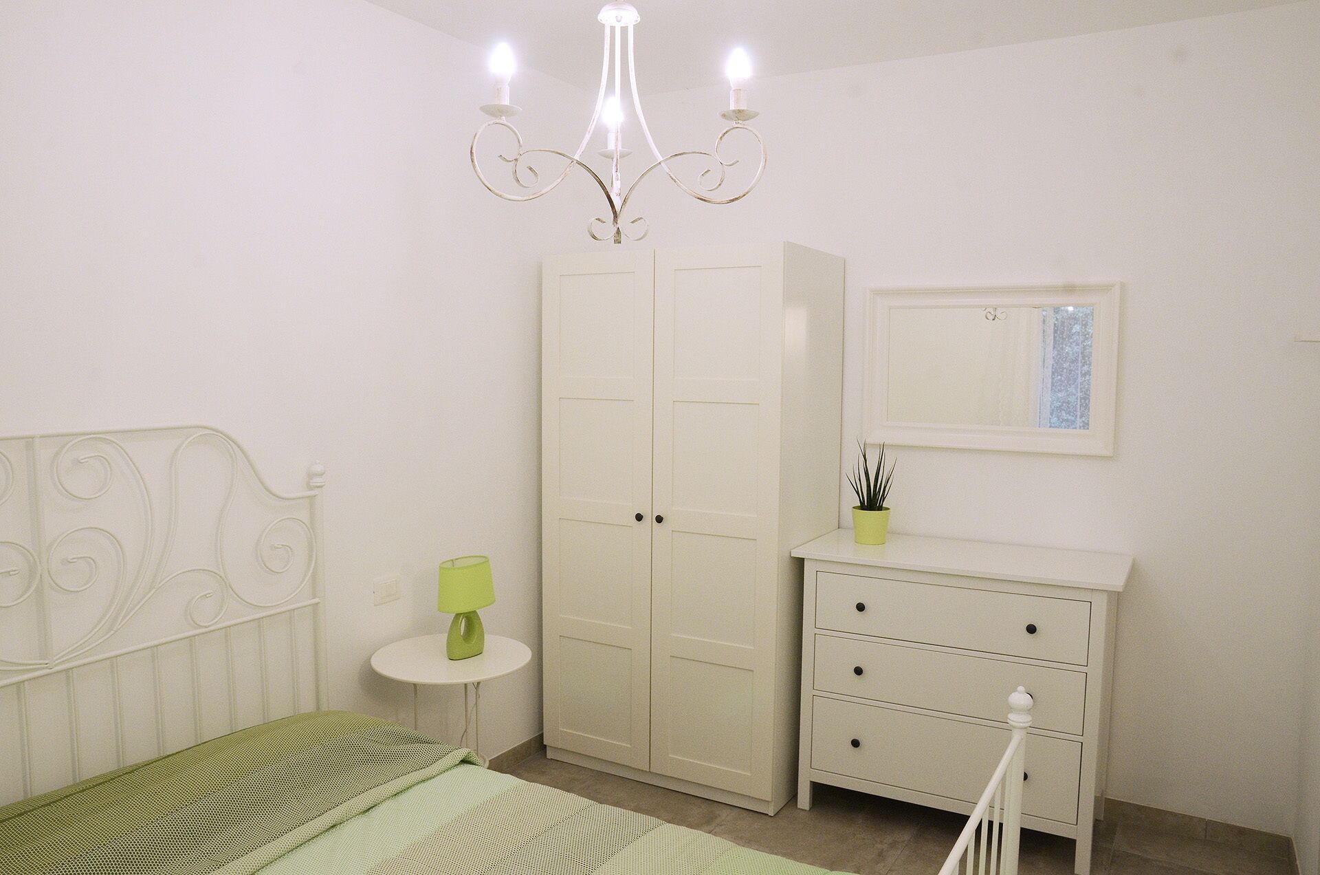 A bedroom with a bed, a wardrobe, a bedside table, a lamp, and a mirror.