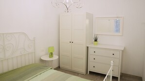 Een slaapkamer met een bed, een kledingkast, een nachtkastje, een lamp en een spiegel.