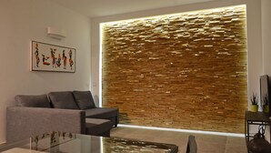 Een moderne woonkamer met een bank, een glazen salontafel en een decoratief wandpaneel.