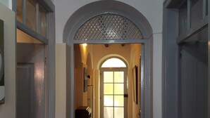 Un couloir doté d’un sol carrelé, une porte au fond et une fenêtre ornée d’un motif en croisillons.