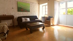Un salon avec un plafond en bois, un canapé, une table basse, un fauteuil en osier et une fenêtre donnant sur un paysage verdoyant.
