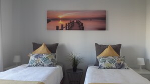 Habitación de hotel con dos camas, cada una con cubrecama blanco y un cojín decorativo. Hay una mesita redonda con una planta en el centro de la habitación.