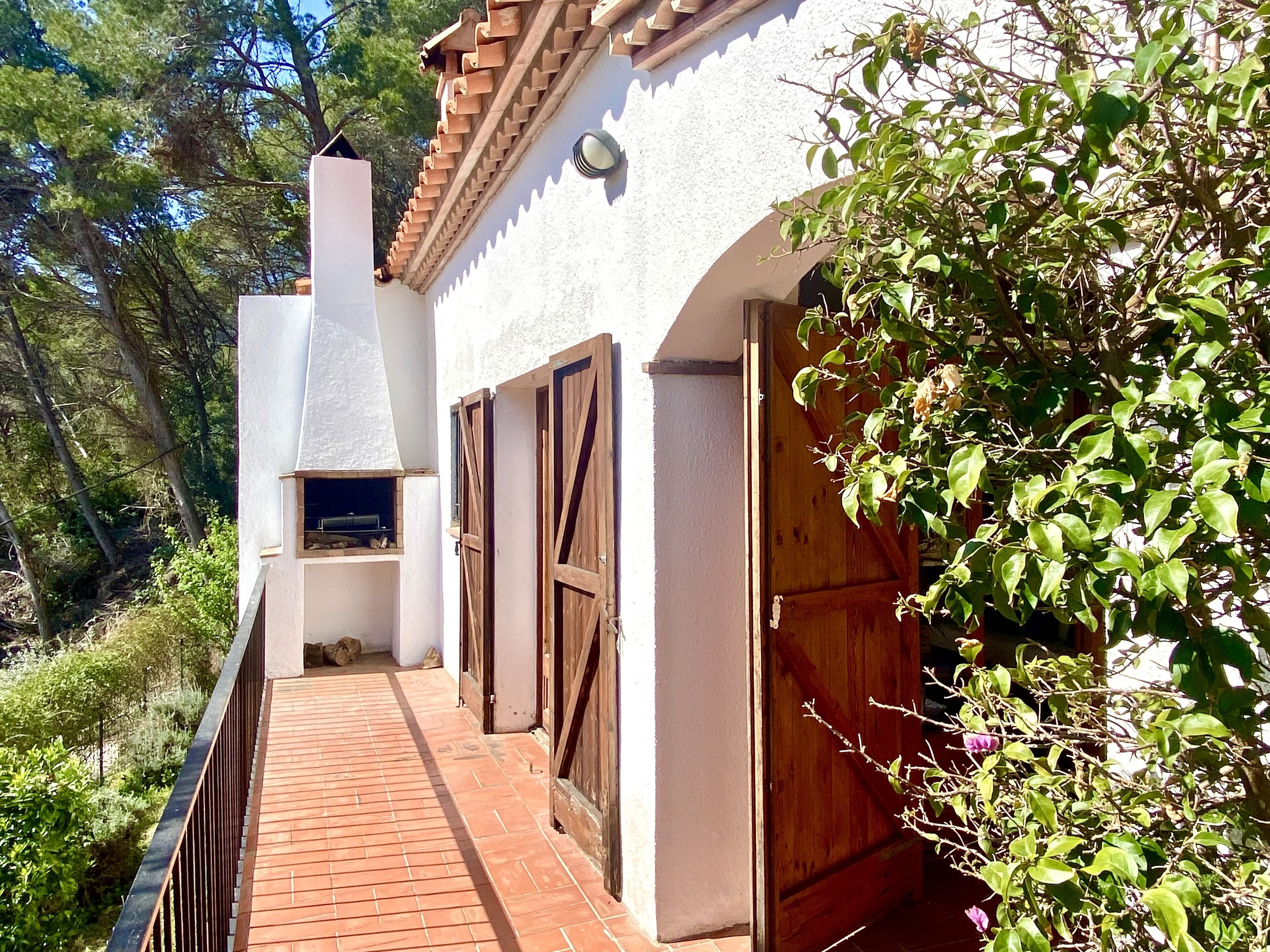 A narrow pathway leading to a white building with a tiled roof and wooden doors.