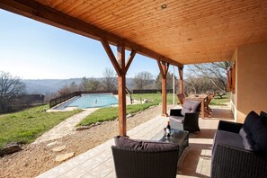 Un patio couvert aménagé avec du mobilier d’extérieur, une piscine et une vue sur le paysage environnant.