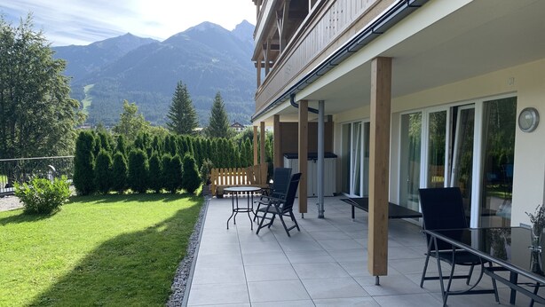 A patio with outdoor furniture, a view of mountains, and a neatly trimmed lawn. - Modern luxury 2 bedroom ground floor apartment with outside terrace and garden (Seefeld)