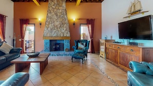 Uma sala de estar acolhedora com lareira de pedra, vigas de madeira no teto, televisão e assentos confortáveis.
