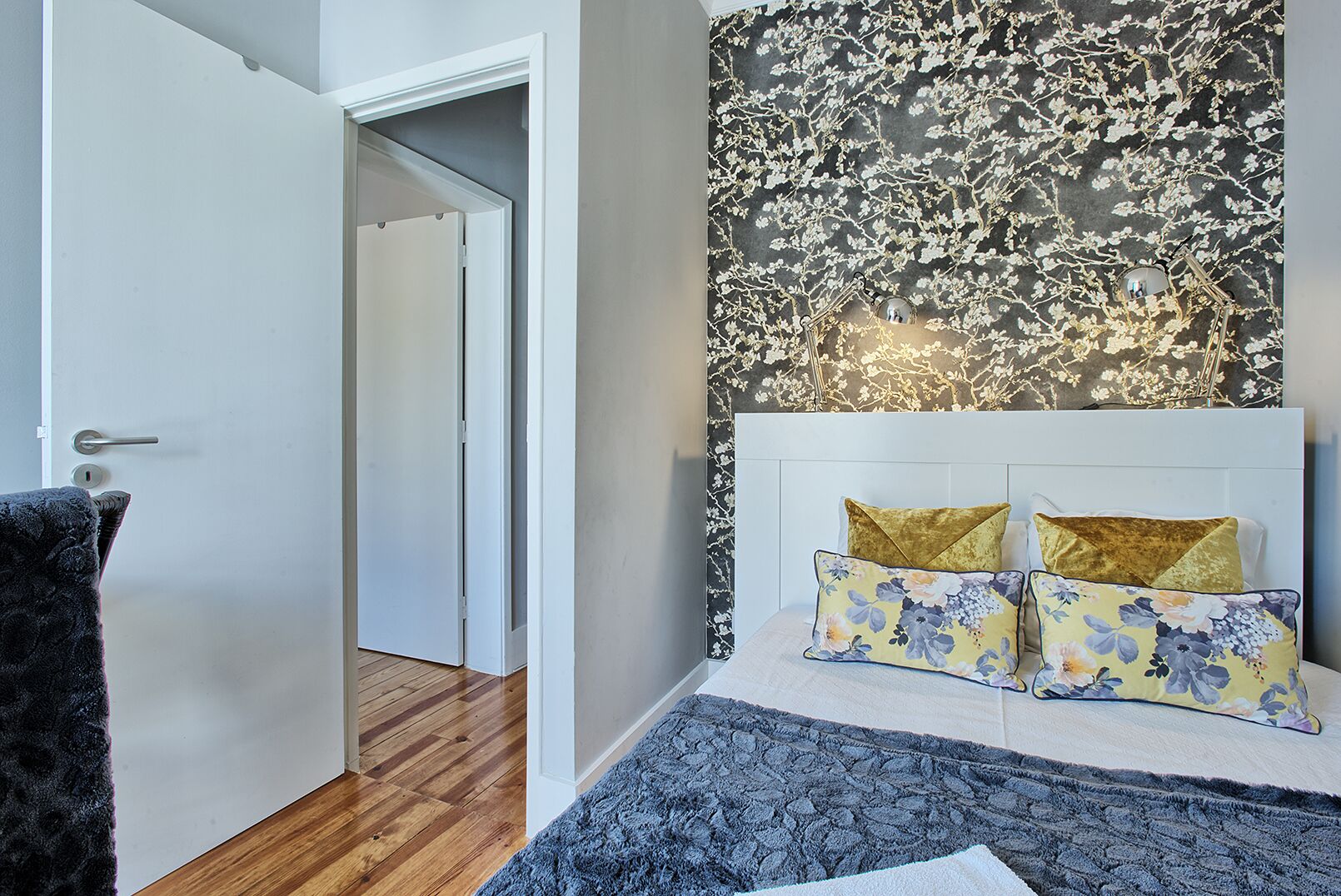 A bedroom with a bed, two pillows, a nightstand, a mirror, and a door leading to another room.