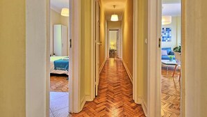 A hallway with a herringbone floor leading to a living area with a blue sofa and a coffee table.