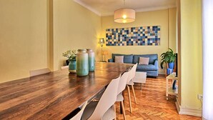 A dining area with a wooden table, chairs, and a blue and white patterned wall behind a sofa.