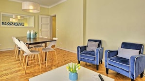 A dining area with a wooden herringbone floor, a white table, and blue chairs.