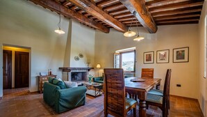 A rustic interior with a fireplace, wooden dining table, and green sofa. - Podere Collelungo 14, Emma Villas (San Casciano dei Bagni)