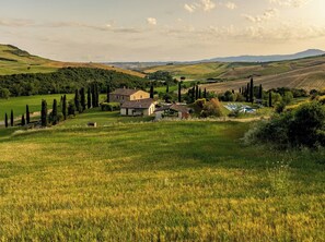 A rural landscape with rolling hills, a farmhouse, and a swimming pool.
