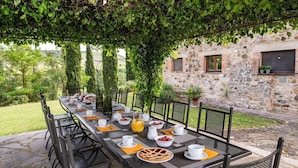 An outdoor dining area with a stone table set for a meal, surrounded by chairs, and a stone wall in the background. - Podere Collelungo 14, Emma Villas (San Casciano dei Bagni)