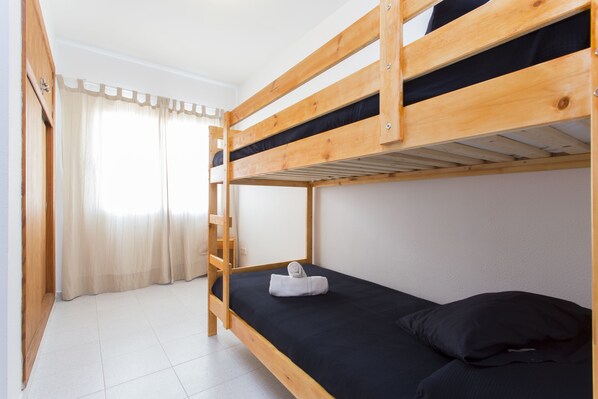 A bunk bed room with a wooden ladder, a black mattress, and a white towel on the lower bunk.