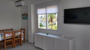 Una habitación con una mesa de comedor, sillas, un ventanal con vistas a un paisaje urbano, un radiador y un televisor montado en la pared.