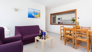 Una sala de estar moderna con un sofá púrpura, una mesa de comedor de madera con sillas y una mesita auxiliar con una botella y vasos.