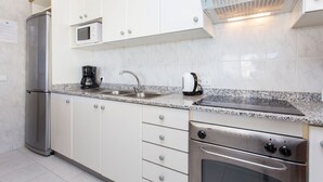 Una cocina moderna con armarios blancos, un refrigerador de acero inoxidable, un microondas, una cafetera, un fregadero y un horno.