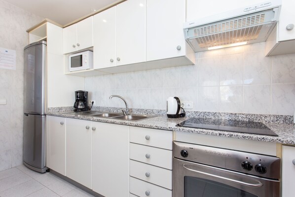 A modern kitchen with white cabinets, a stainless steel refrigerator, a microwave, a coffee maker, a sink, and an oven.