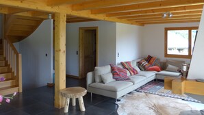 A modern living room with a wooden ceiling, a staircase, a sofa with colorful cushions, a small wooden stool, and a rug. - Crans Montana - Large and modern chalet with stunning views in a quiet setting (Randogne)
