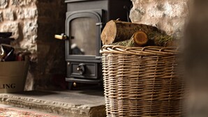 Ein rustikaler Innenraum mit einer Steinwand, einem Korbwesen mit Holzscheiten und einem alten Kochherd.