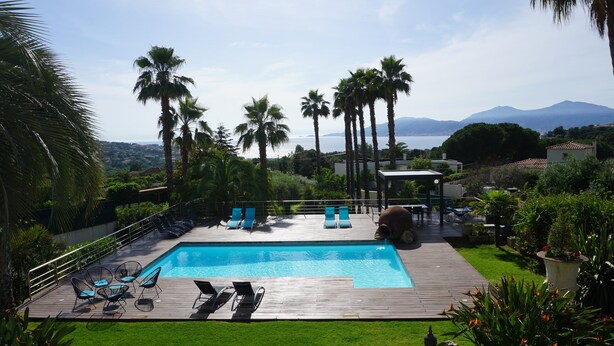 Ein Poolbereich mit Liegestühlen, einer Holzterrasse und Blick auf das Meer und die Berge.