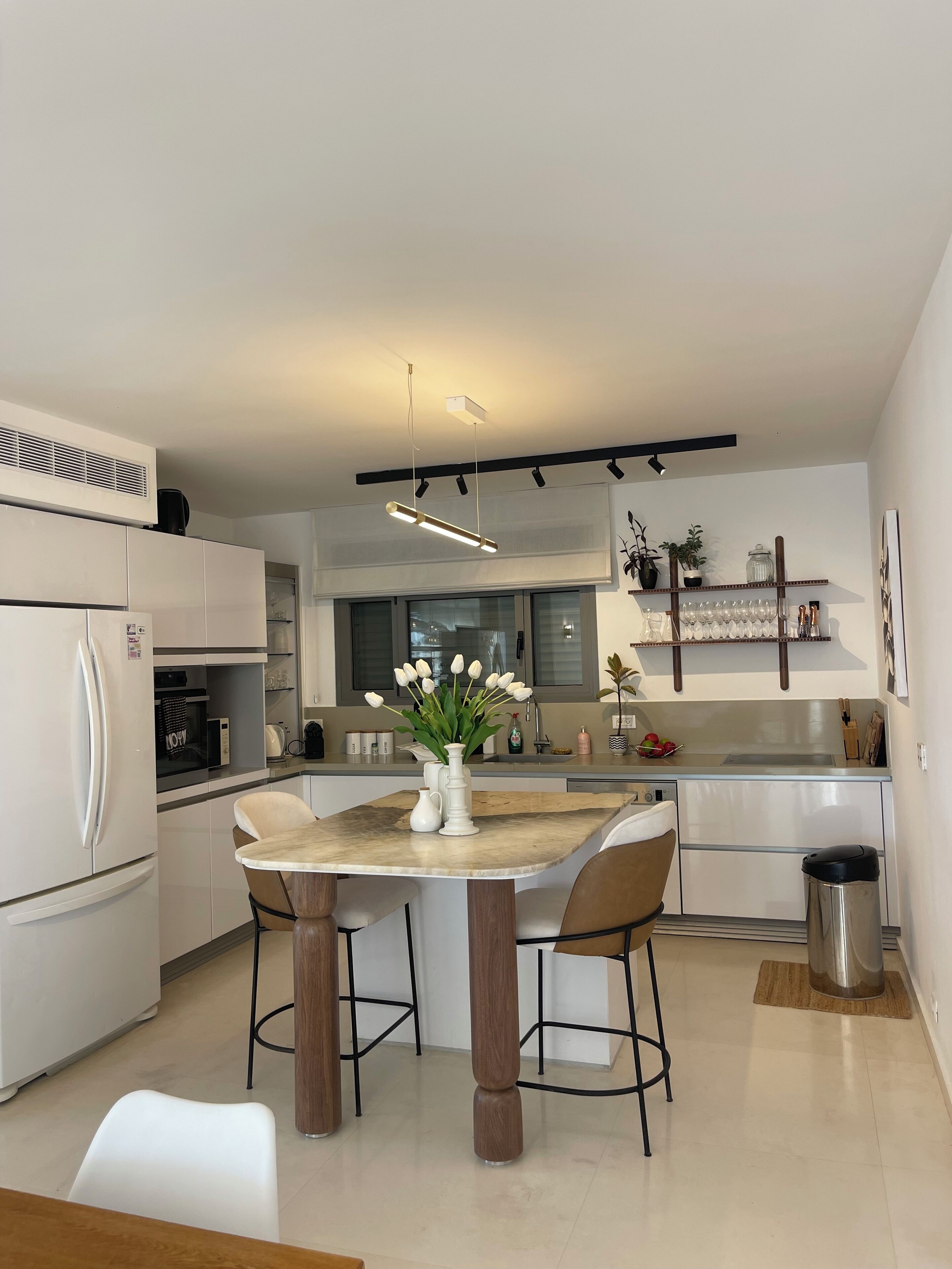 A modern kitchen with white cabinetry, a central island with chairs, a vase of tulips, and a hanging light fixture.