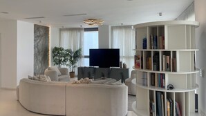 Ein modernes Wohnzimmer mit einem Ecksofa, einem Flachbildfernseher, einem Bücherregal und einem großen Fenster mit Vorhängen.