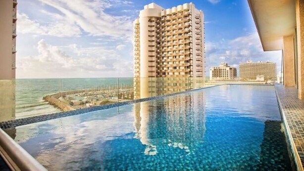 Ein Hotelpool mit klarem, blauem Wasser, umgeben von Hochhäusern und Blick auf den Ozean.