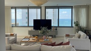 Ein modernes Wohnzimmer mit großem Fernseher, zwei Sofas, einem Couchtisch und Meerblick durch große Fenster.