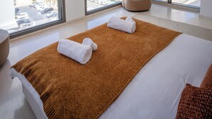 Ein modernes Hotelzimmer mit einem großen Bett, Blick auf die Stadt und einer runden Deckenleuchte.